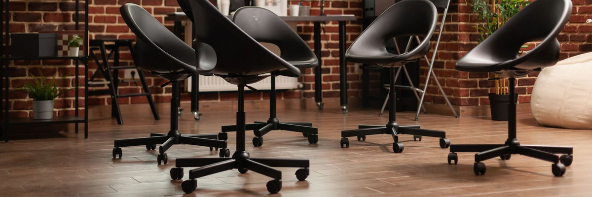 Fünf moderne schwarze Bürostühle auf einem Holzboden in einem Raum mit Backsteinwänden.