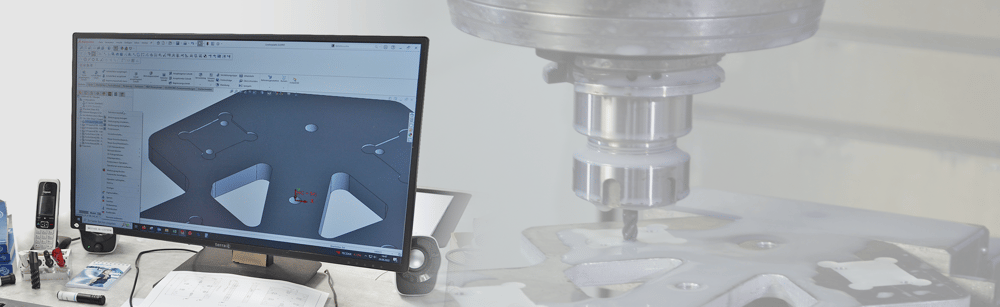 Computerbildschirm mit einem 3D-CAD-Modell; im Hintergrund fräst eine CNC-Maschine ein Metallteil.