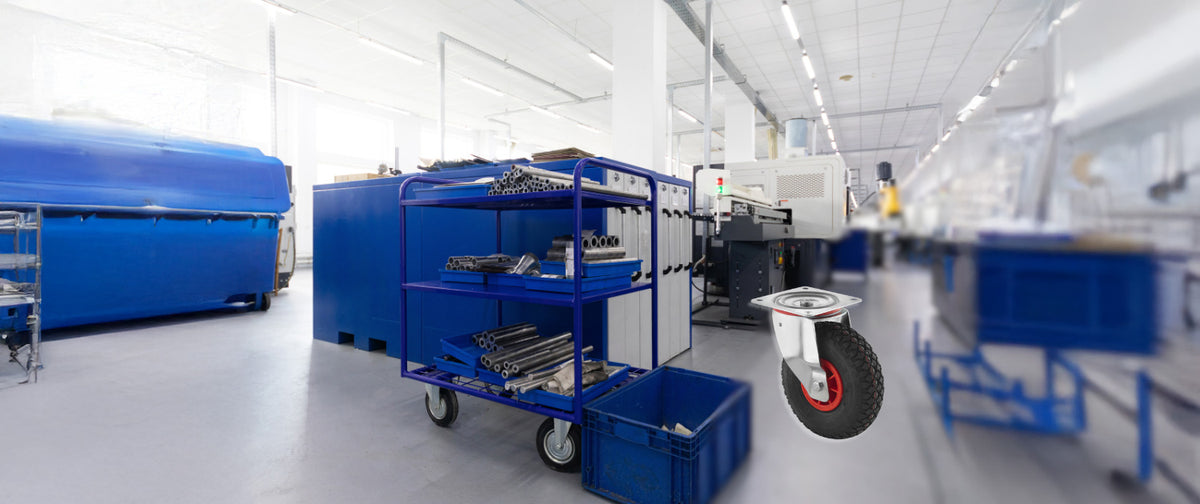 Blauer Metallwagen mit Metallstangen in einer hellen Fabrikhalle; rechts ist ein großes Lenkrollrad zu sehen.