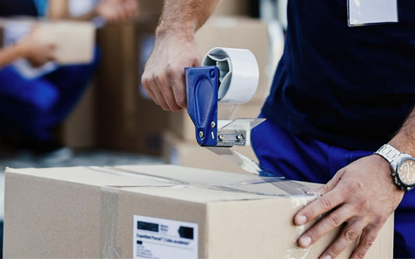 Eine Person, die einen Karton mit durchsichtigem Verpackungsklebeband mithilfe eines Klebebandspenders verschließt.
