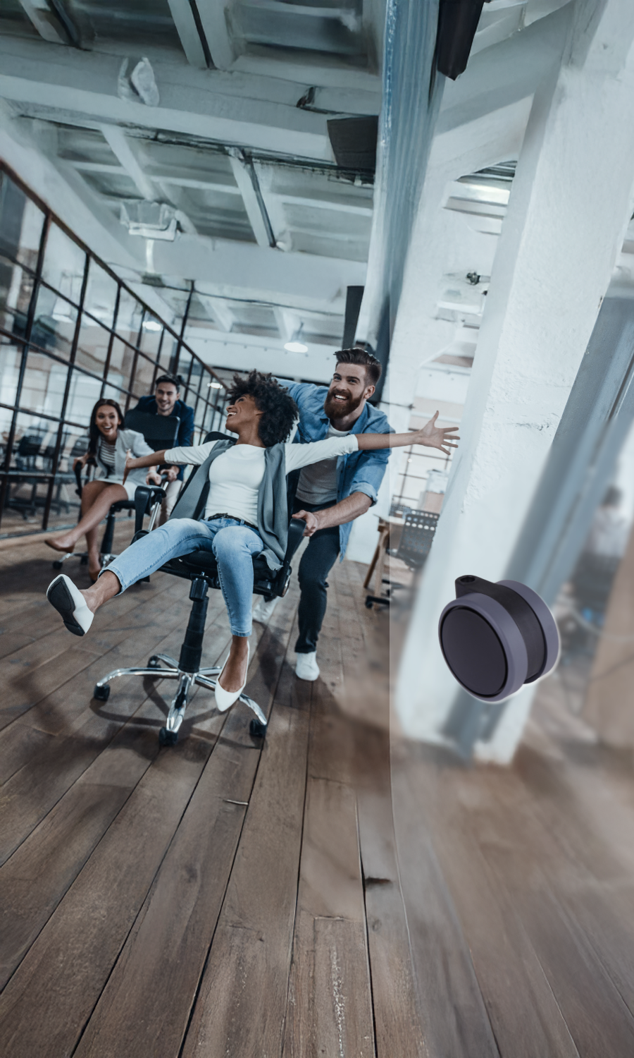Vier Personen in einem Büro, zwei davon schubsen spielerisch eine Frau auf einem Stuhl hin und her, alle lächeln und lachen.