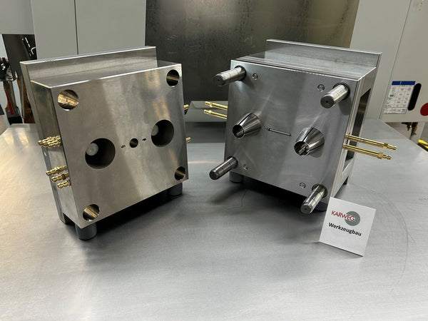 Zwei Metallformblöcke mit Stiften und Löchern, ausgestellt auf einem Metalltisch zusammen mit einer Visitenkarte.
